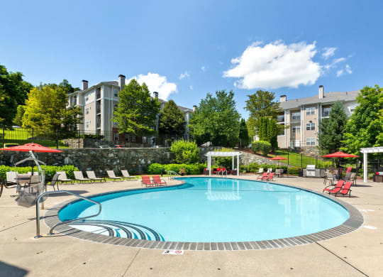 a swimming pool with red chairs and umbrellas and a building in the background