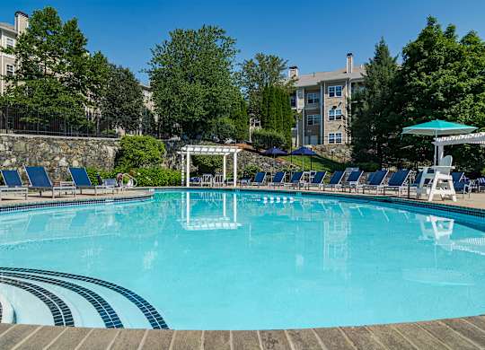 A large swimming pool with a stone wall and sun loungers.