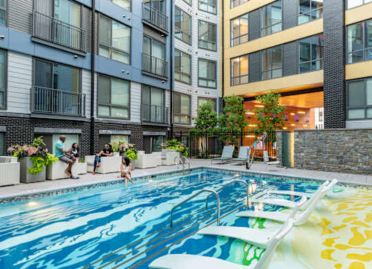 A swimming pool in a residential building with people relaxing by the poolside.