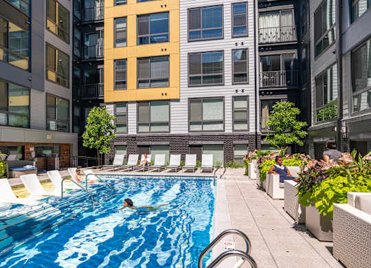A person is swimming in a pool surrounded by chairs and plants.