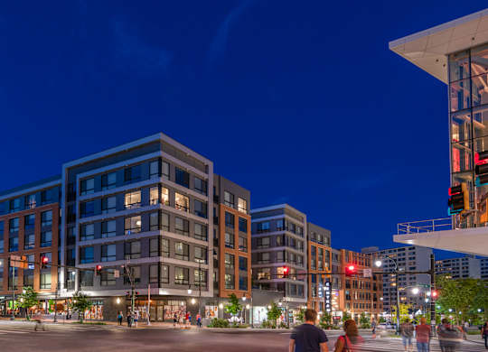 A city street at night with people walking and buildings with lit up windows.