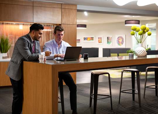 Two men are working on laptops in a modern office setting.