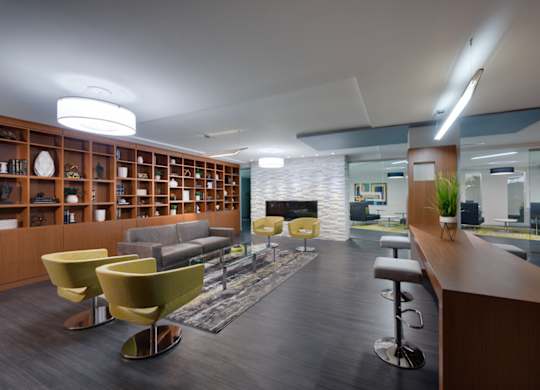 A modern office space with a long wooden bookshelf and yellow chairs.