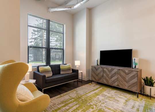 A living room with a yellow chair, a black couch, and a flat screen TV.