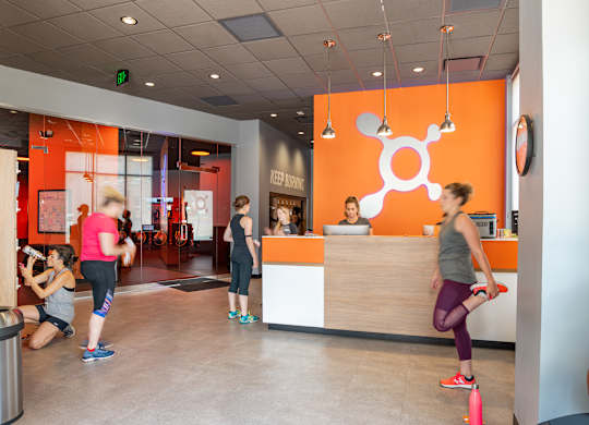 A gym with orange walls and people exercising.