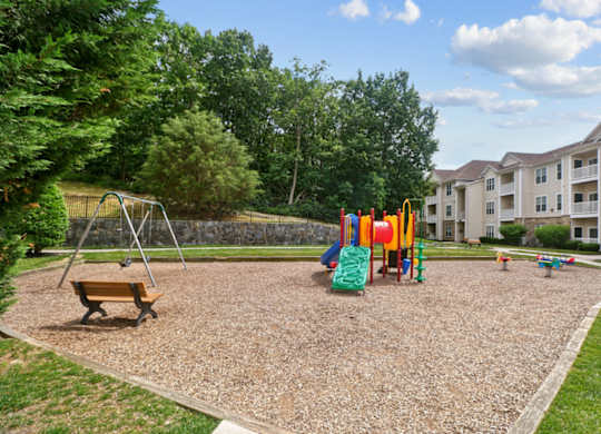 A playground with a swing set and a slide in the foreground and apartment buildings in the background.