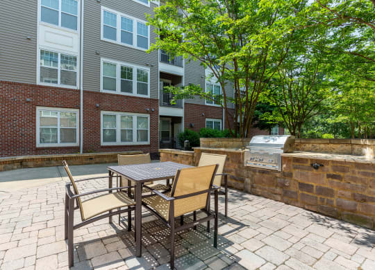 a patio with a table and chairs and a grill in front of a brick building