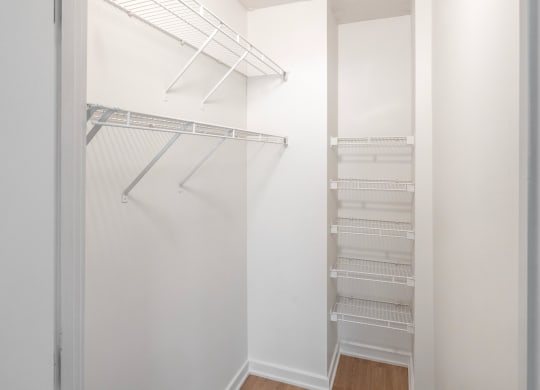 a walk in closet with white walls and shelves and a mirrored closet door