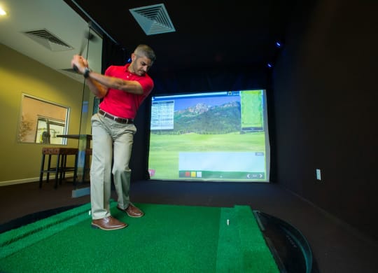 a man in a red shirt is swinging a golf club at a golf ball