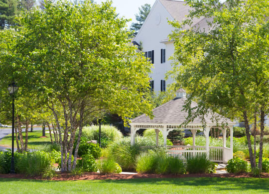 a white gazebo in a park with a house in the background