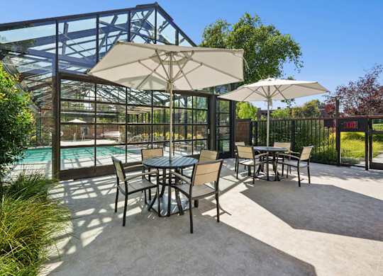 Outdoor patio seating with umbrellas beside the enclosed community pool.