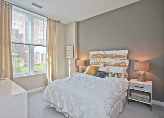 a bedroom with a large window and a bed with a white comforter