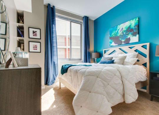 a bedroom with a blue accent wall and a bed with a white comforter