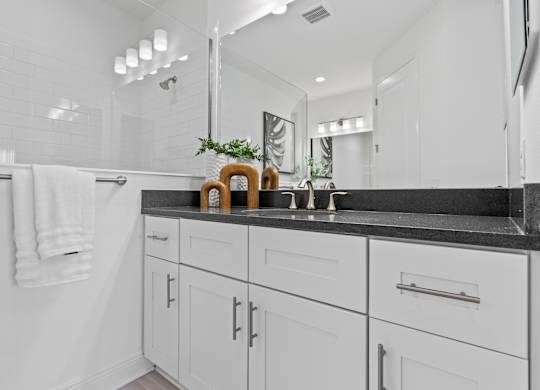A white bathroom with a black counter top and a white towel hanging on the wall at Marisol in Lakewood Ranch, FL