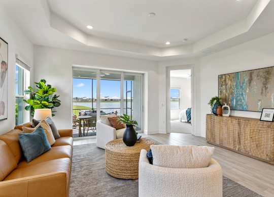 A living room with a tan couch, a white chair, and a wooden cabinet at Marisol in Lakewood Ranch, FL