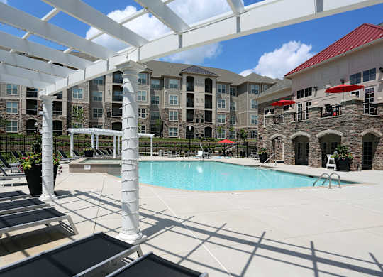 A pool area with a white pergola and a stone building in the background.