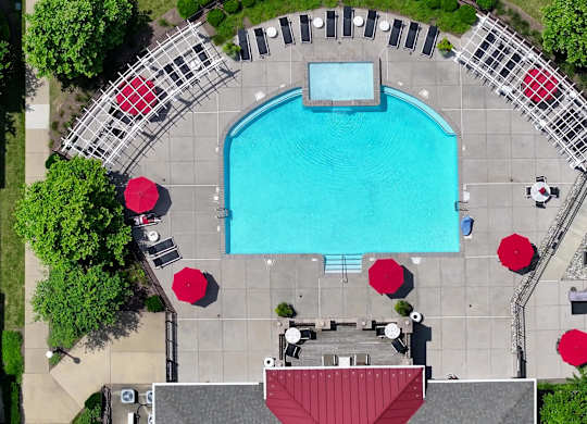 An aerial view of a swimming pool surrounded by red umbrellas and lounge chairs.