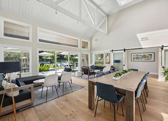 Clubhouse dining area with long wood table, blue accent mural wall, and adjacent kitchen