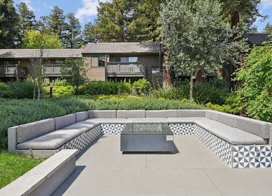 Outdoor fire pit with built-in seating and surrounding greenery at Old Orchard Apartments