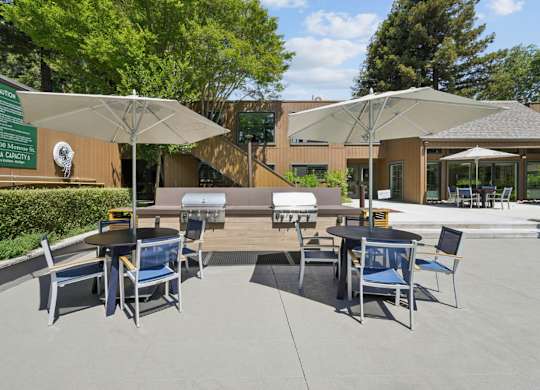 Outdoor grilling area with gas grills, dining tables, umbrellas, and poolside seating at Old Orchard Apartments