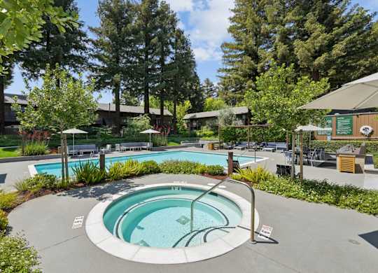 Outdoor hot tub with surrounding seating, landscaping, and pool area at Old Orchard Apartments