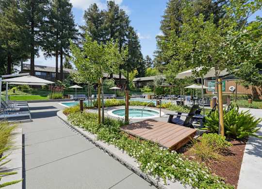Pool area with hot tub, lounge chairs, umbrellas, and landscaped greenery