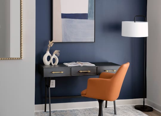 A desk with a chair and a lamp in front of a blue wall.