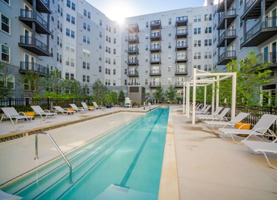 a pool with lounge chairs next to an apartment building