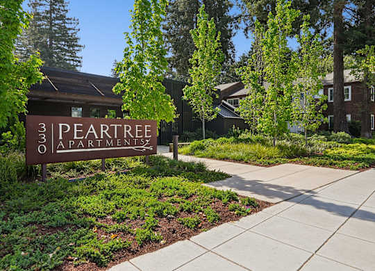 A brown sign with the words "31 PEAR TREE Apartments" in front of a building.