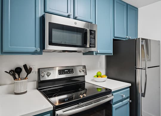 A kitchen with blue cabinets and a stainless steel oven and microwave.