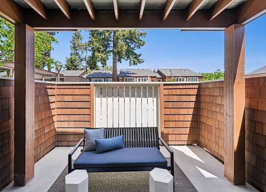 A blue couch is on a patio with a white fence in the background.