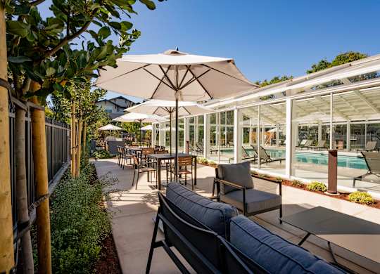 Outdoor seating area with sofas and umbrellas beside indoor pool