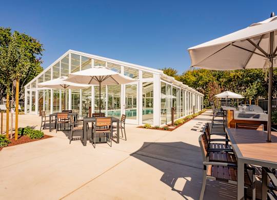 Outdoor dining tables with umbrellas next to indoor pool building