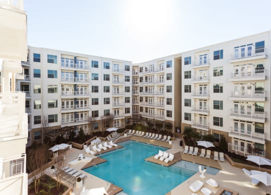 an overhead view of a large pool with white lounge chairs and umbrellas in front of
