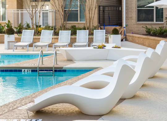 a row of white chaise lounges sit next to a swimming pool