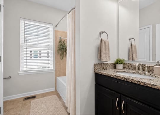 Bathroom with bathtub and shower, granite countertop, and window with blinds.