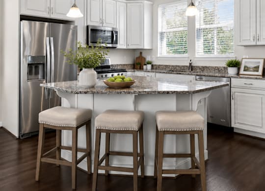 Modern townhome kitchen with white cabinets, granite countertops, stainless steel appliances, and large windows.
