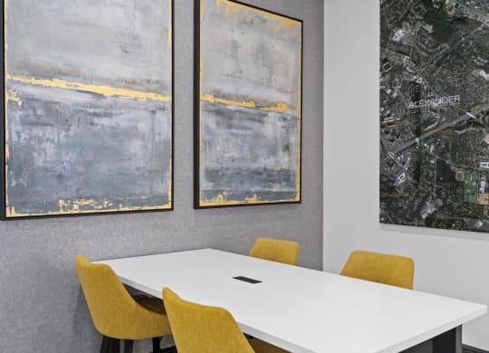 a white table with yellow chairs and paintings on the wall