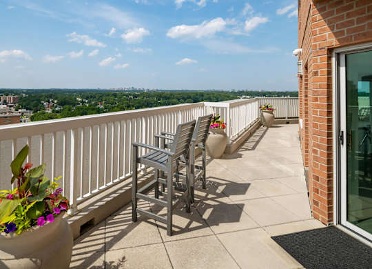 A balcony with a chair and a potted plant overlooking a cityscape.