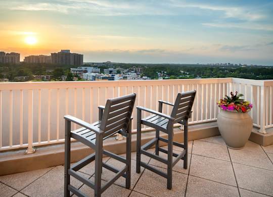 Two chairs are on a balcony with a sunset view.