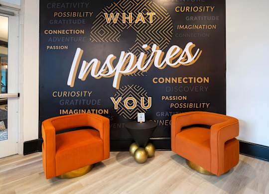Two orange chairs are in front of a black wall with words that inspire.