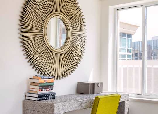 A desk with a yellow chair and a large circular mirror above it.