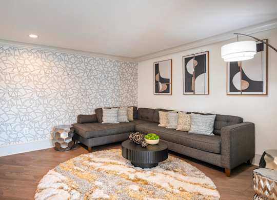 A living room with a grey couch, a coffee table, and a patterned wallpaper.