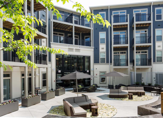 a courtyard with couches and umbrellas in front of an apartment building