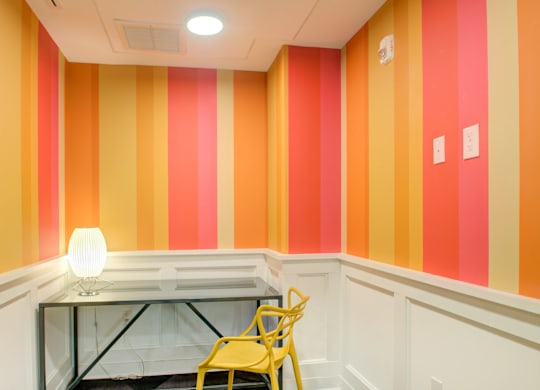 A yellow chair is in front of a desk with a lamp on it.