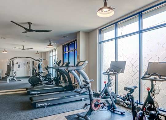 A gym with treadmills, exercise bikes, and a fan.