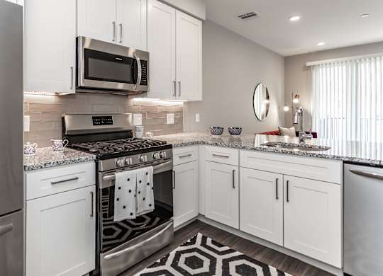A modern kitchen with white cabinets and a black and white patterned rug.