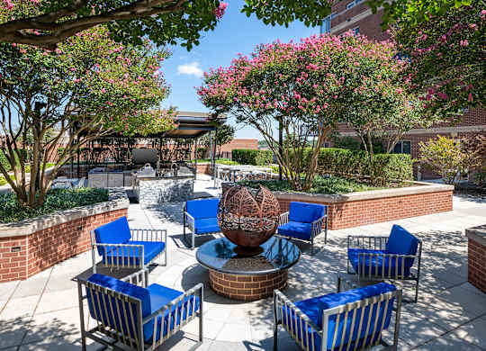 Landscaped Vantage Mosaic courtyard with blue cushioned chairs arranged around a decorative metal fire feature.