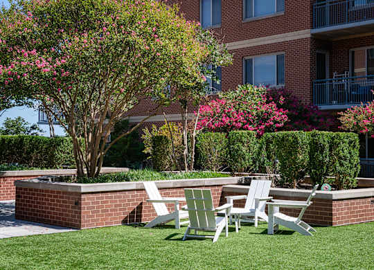 Green courtyard lawn with white Adirondack chairs, flowering trees, trimmed hedges and brick apartment balconies.