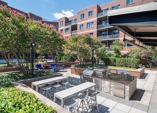 Courtyard kitchen with stainless steel grills, stone counters, bar seating, dining tables and apartment balconies beyond.